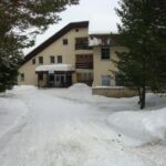 Budova zariadenia Guliak v zimnom období obklopená vysokými smrekmi a bohatou snehovou nádielkou.