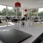 Reštaurácia v zariadení Signál. Pohľad na priestrannú, presvetlenú miestnosť s veľkými oknami, s elegantnými stolmi a stoličkami, moderrne dekorovanú vo farbách biela, čierna a červená.