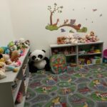 Detský kútik zariadenia SNV s policami plnými hračiek, dekoráciou na stene a kobercom pre znázorňujúcim mesto, ideálnym na hru s autíčkami.